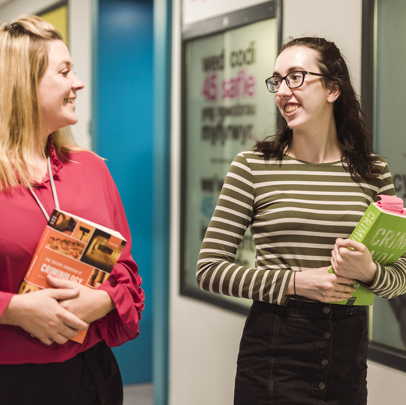 Criminology lecturer walking with a student carrying criminology textbooks